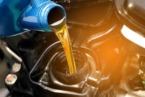 Oil being poured into a motorcycle engine's oil fill port from a blue container. | Torque European Car Care