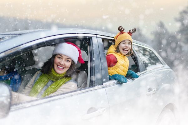 Woman and child in festive attire smile from car in a snowy scene. | Torque European Car Care
