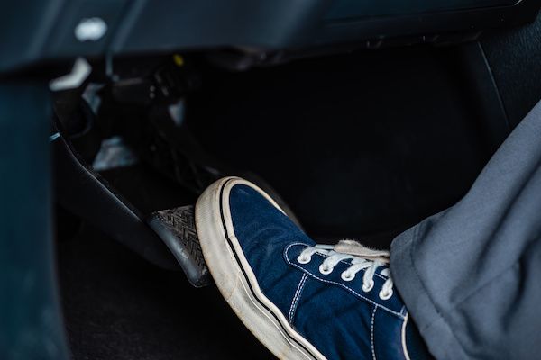 Foot in blue shoe pressing a car's brake pedal. Interior view, dark setting. | Torque European Car Care