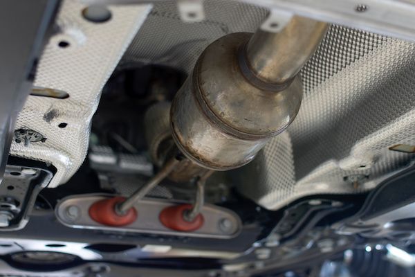 Undercarriage view of a car's exhaust system with catalytic converter, pipes, and heat shields. | Torque European Car Care