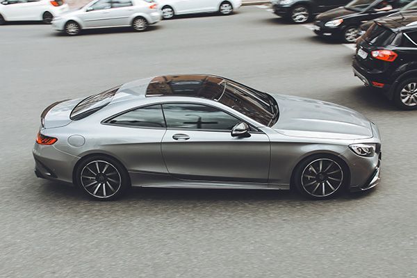 Silver Mercedes coupe driving on a paved street with other cars parked nearby. | Torque European Car Care