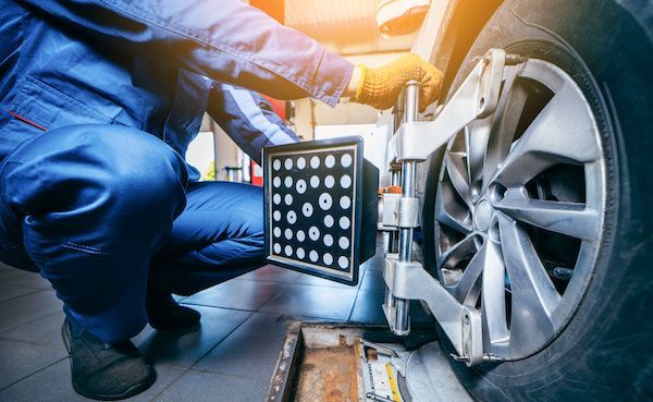 Mechanic in blue overalls aligning a car wheel with a measuring device in a garage. | Torque European Car Care
