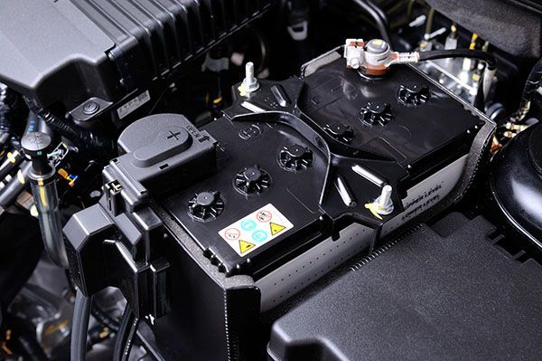 Car battery, black plastic case, in engine bay, with terminals and warning labels. | Torque European Car Care