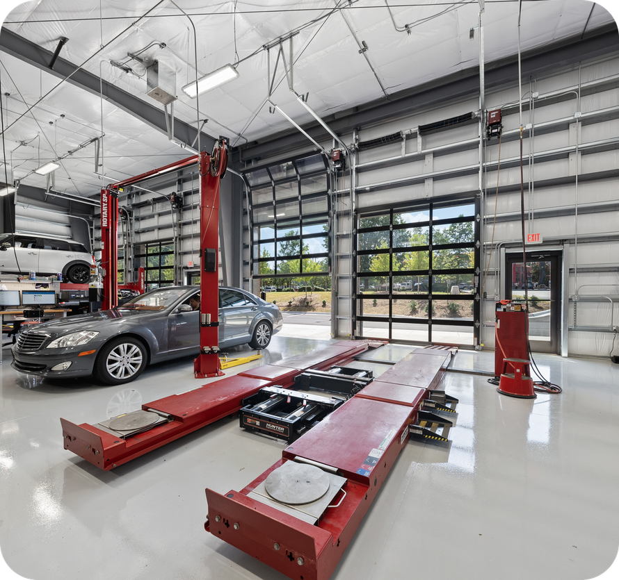 Bright auto repair shop with gray car on lift, red lifts, open glass garage door. | Torque European Car Care