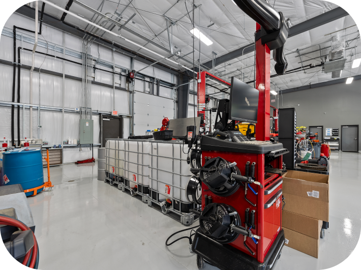 Red wheel alignment machine in a well-lit auto shop with white tanks, blue barrel, and metal beams. | Torque European Car Care