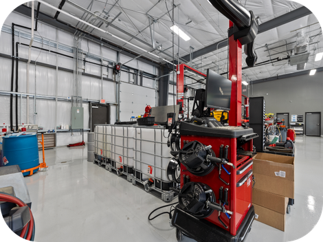 Red wheel alignment machine in a well-lit auto shop with white tanks, blue barrel, and metal beams. | Torque European Car Care