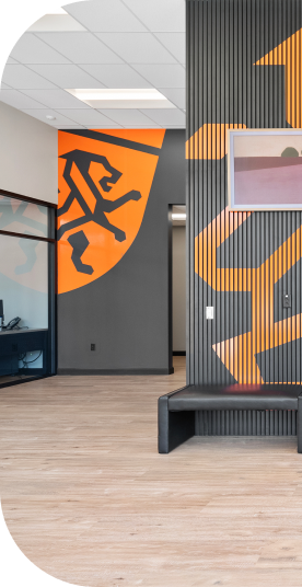 Modern office entryway with orange and black accents, wooden floor, bench, artwork. | Torque European Car Care