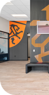 Modern office entryway with orange and black accents, wooden floor, bench, artwork. | Torque European Car Care