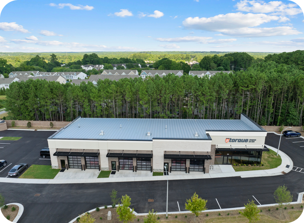 Aerial view of a modern auto repair shop with black garage doors, set against a backdrop of trees and houses. | Torque European Car Care