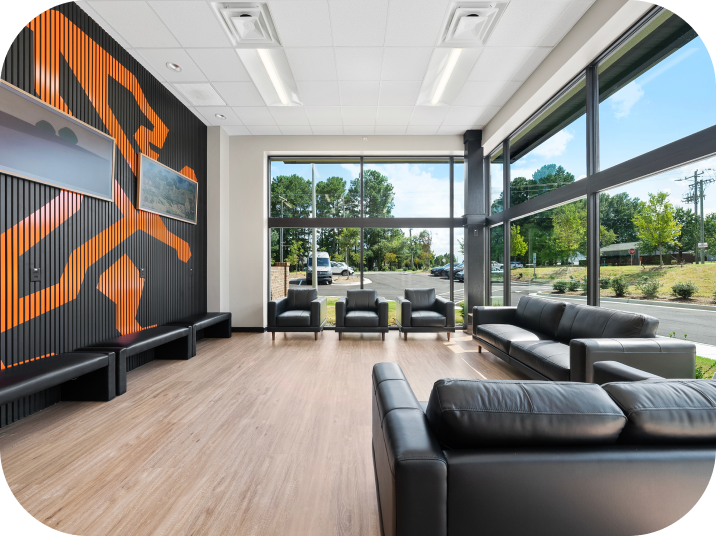 Modern waiting room with black couches and chairs, large windows overlooking a street. Orange logo on the wall. | Torque European Car Care