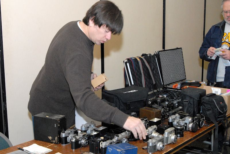 Woman in straw hat smiles, holding wine glass near a lake.