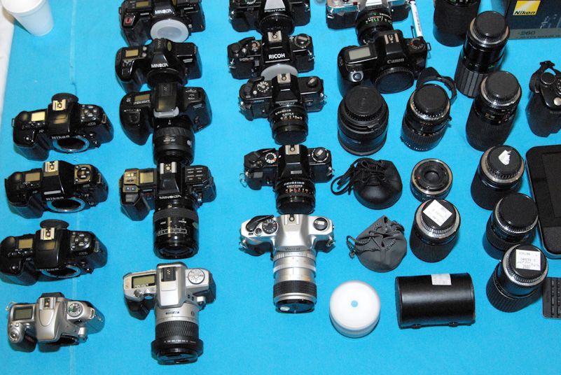 Woman in straw hat smiles, holding wine glass near a lake.