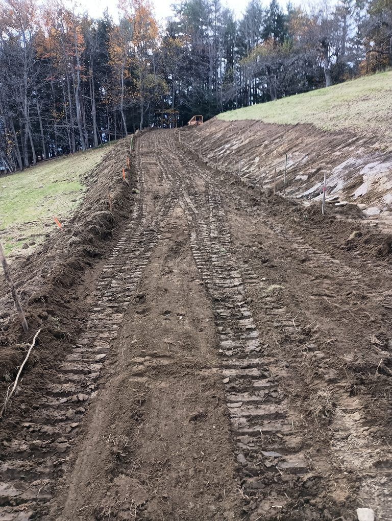 A yellow excavator is driving down a dirt road.