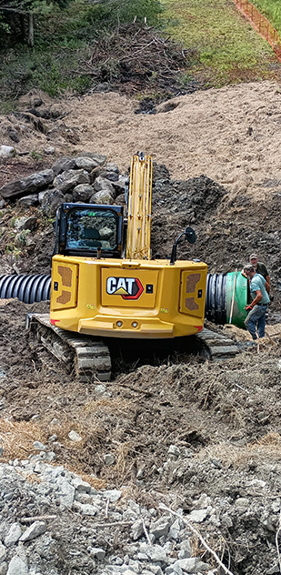 A yellow excavator is sitting in the dirt next to a green pipe.