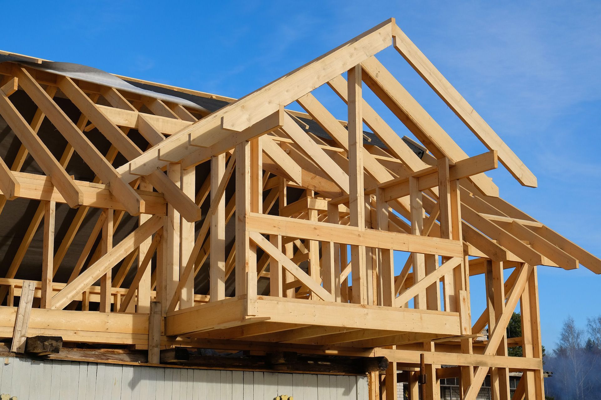 A wooden house is being built with a blue sky in the background.