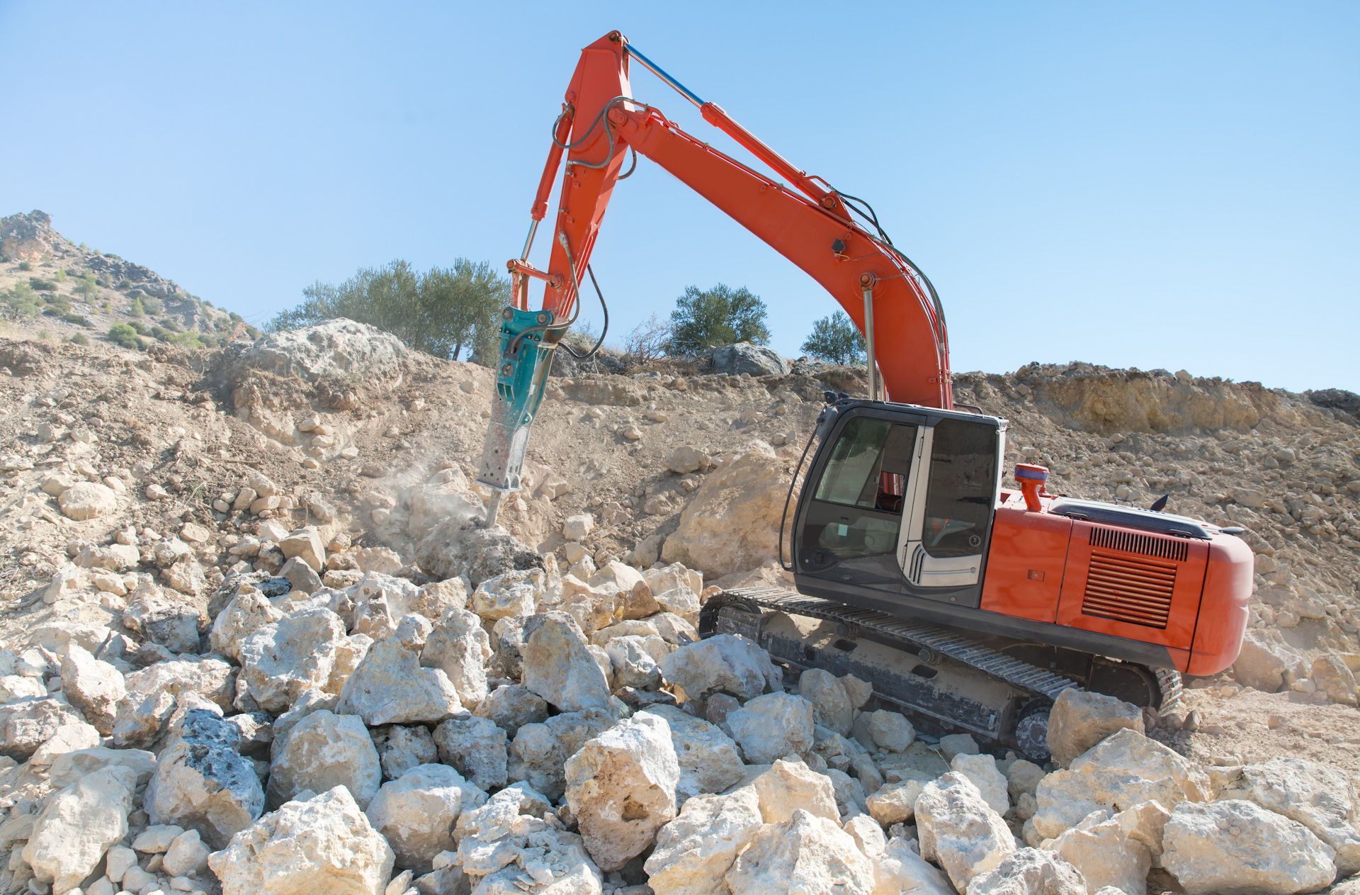 A large orange excavator is breaking rocks in a quarry