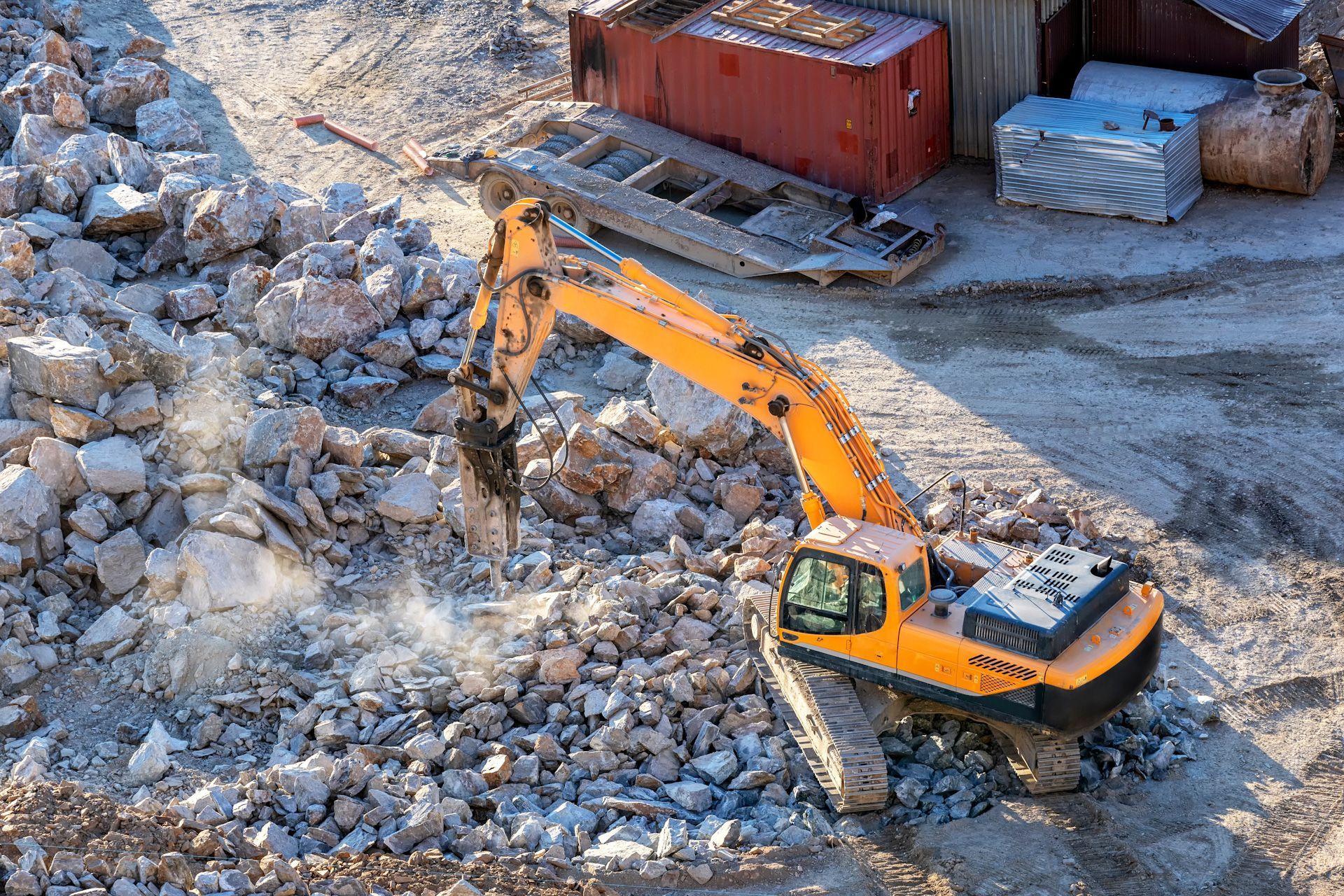 A yellow excavator is working on a pile of rocks.