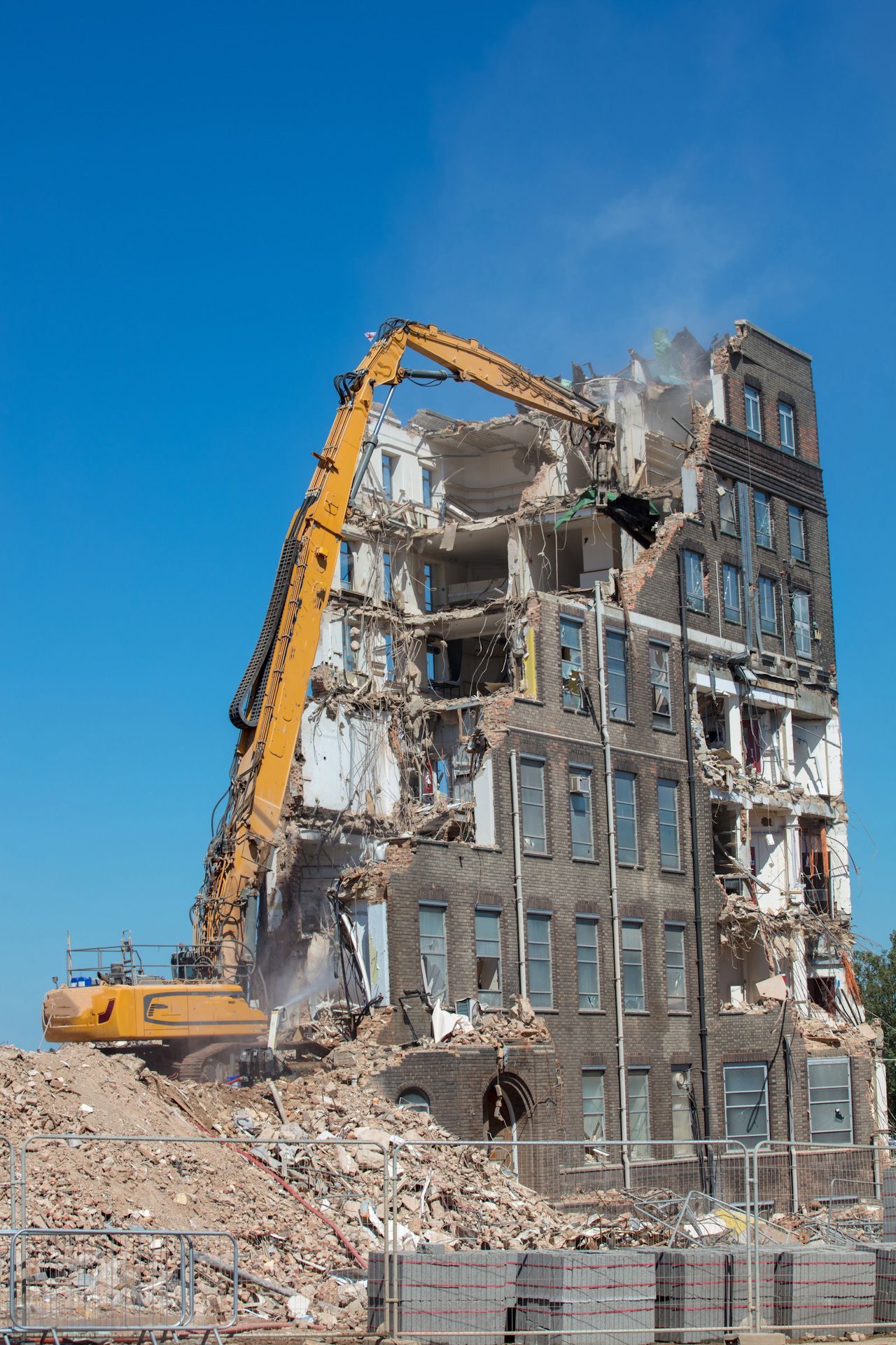 A large building is being demolished by a yellow excavator.