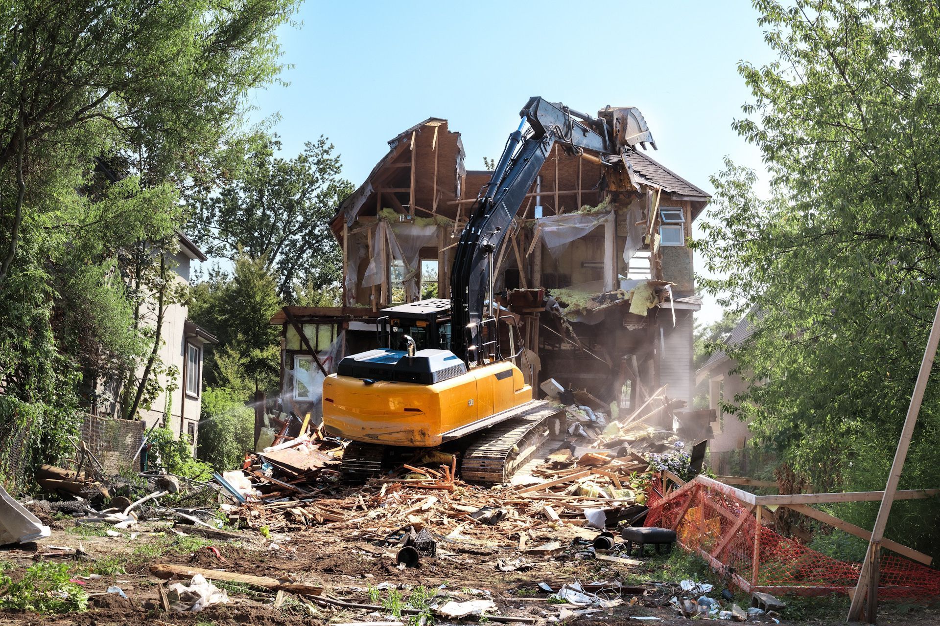 A large yellow excavator is demolishing a house.