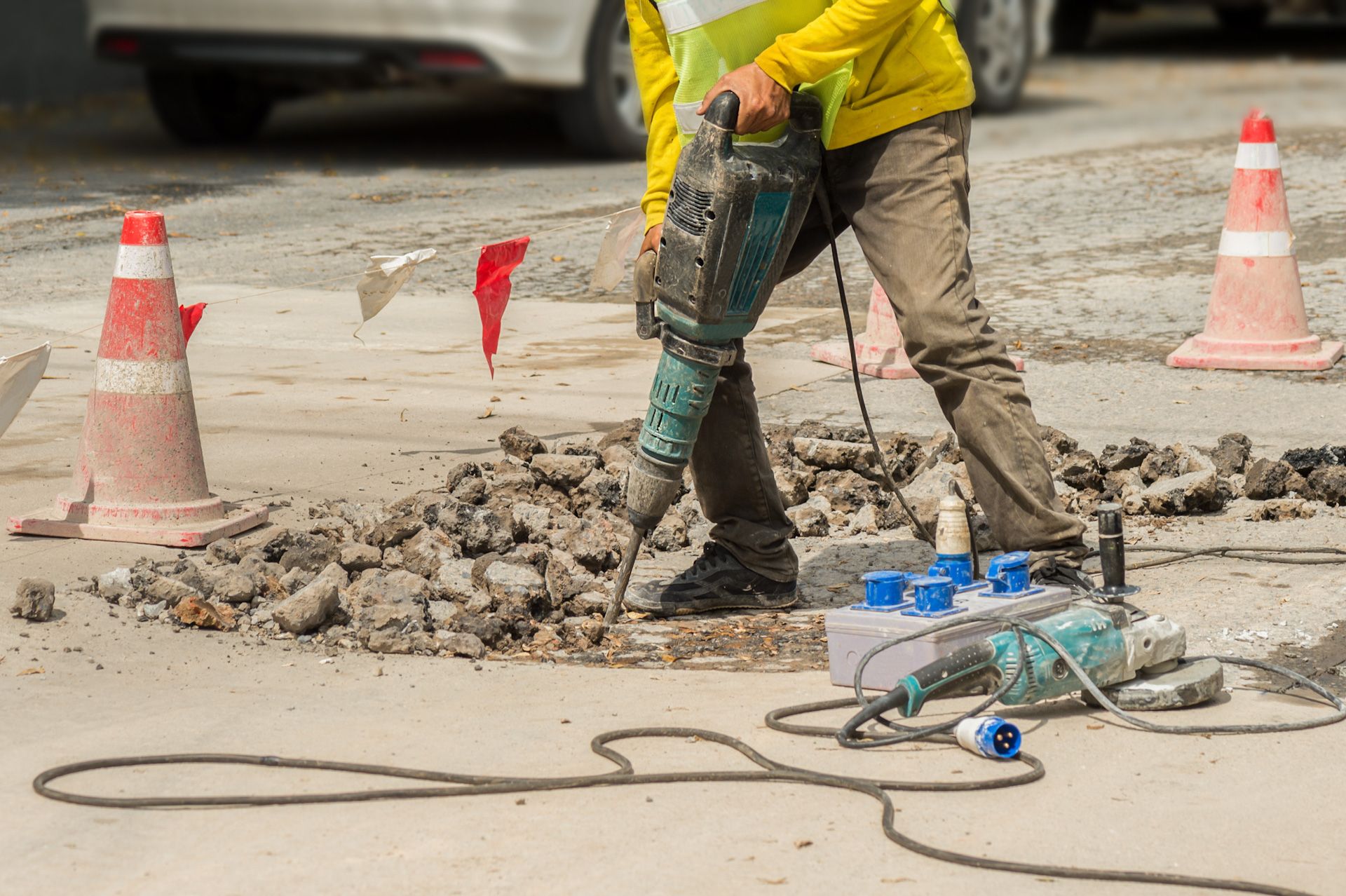 A construction worker is using a hammer drill to drill a hole in the ground.