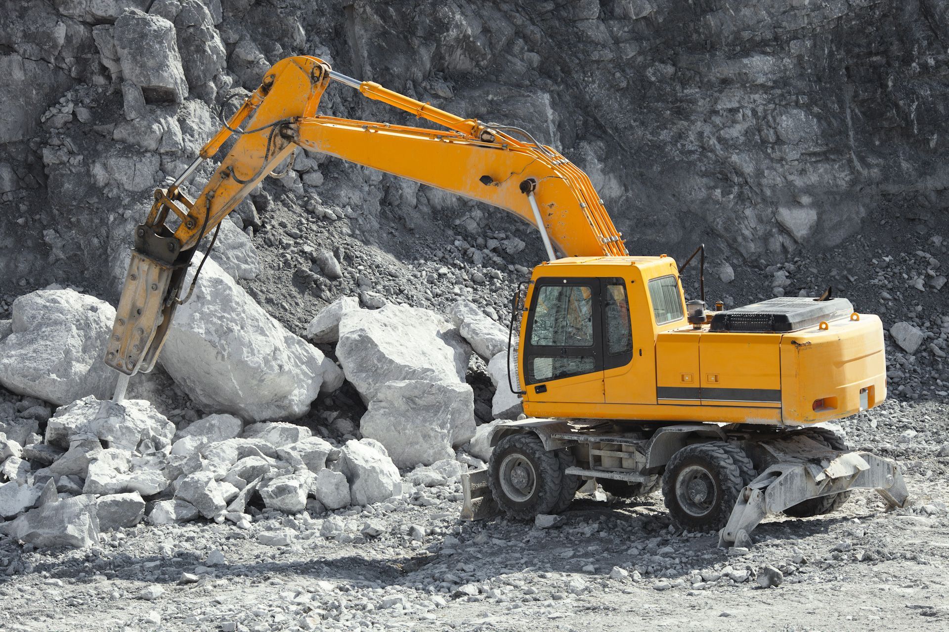 A yellow excavator is moving rocks in a quarry.