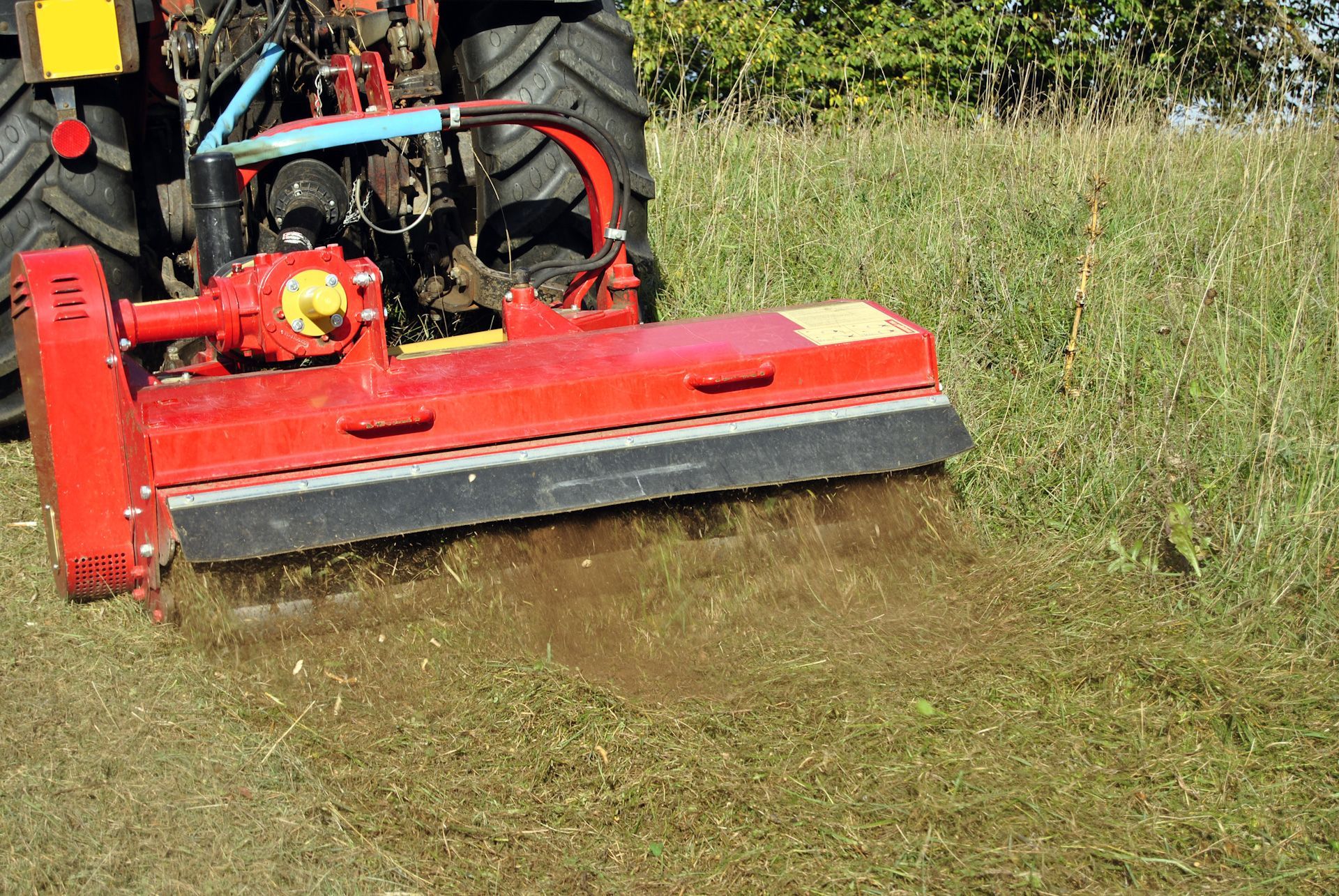 A red tractor is mowing a grassy field with a machine.