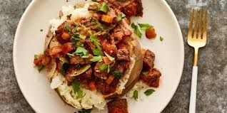 Pulled chicken sandwich on a bun, topped with cheese and parsley, on a white plate.
