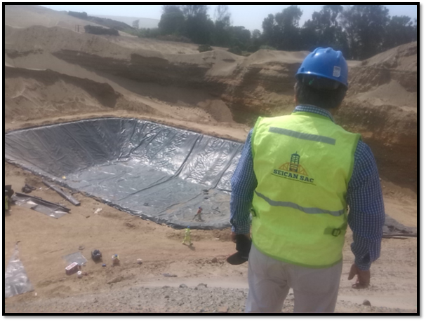 Un hombre que lleva un casco y un chaleco amarillo está parado frente a una piscina grande.