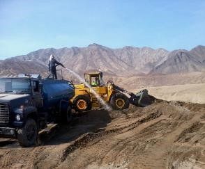Un hombre está parado encima de un camión rociando agua sobre una excavadora.