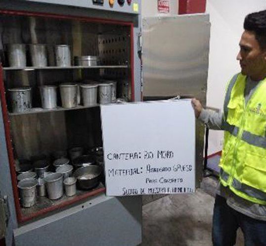 Un hombre con un chaleco amarillo sostiene un cartel frente a un gabinete.