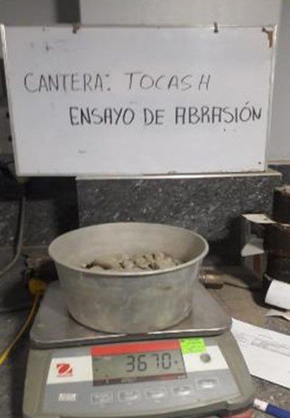 Un recipiente de hormigón se encuentra sobre una báscula junto a un cartel que dice cantera tocash ensayo de abrasión