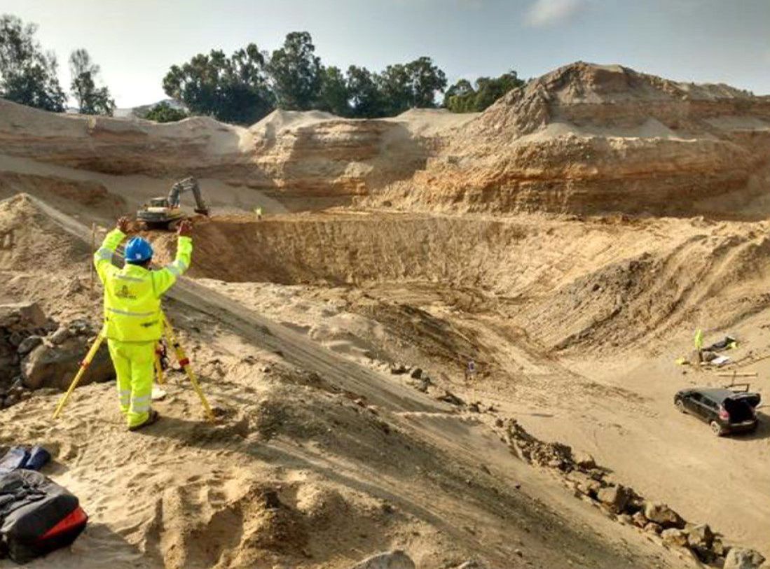 Un hombre con una chaqueta amarilla está parado en medio de un campo de tierra.