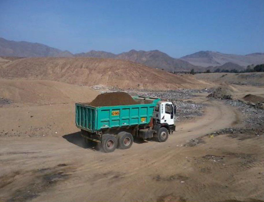 Un camión volquete circula por un camino de tierra con montañas al fondo.