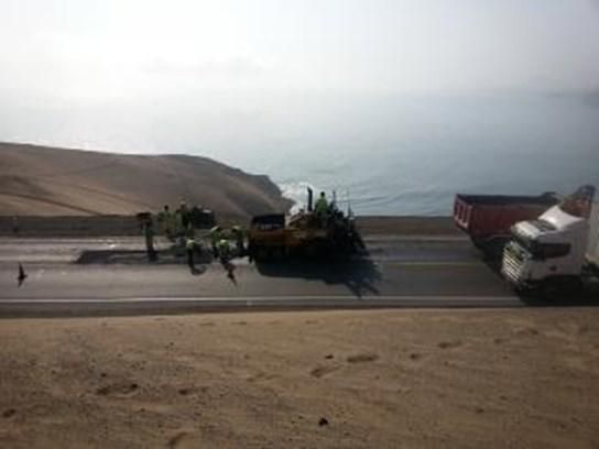Dos camiones circulan por una autopista al lado de un cuerpo de agua.
