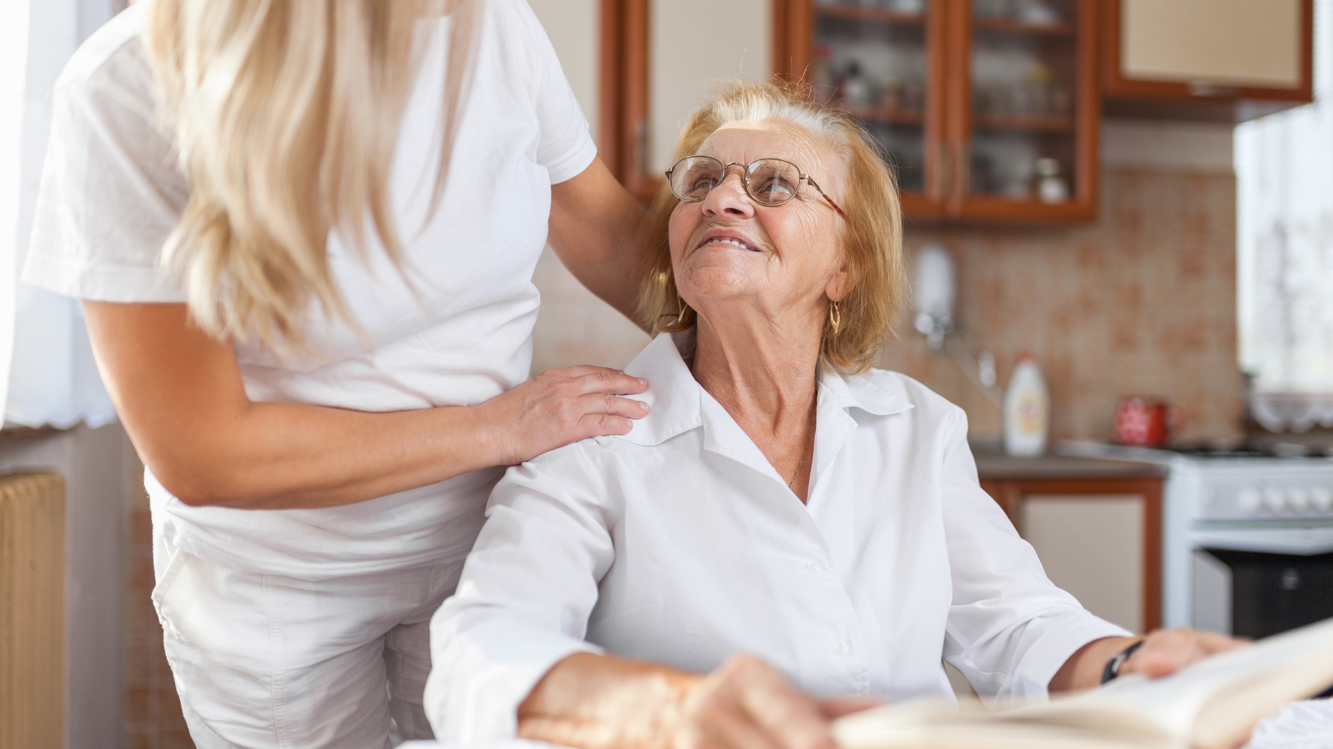 Young caregiver comforting an elderly woman in a bright kitchen