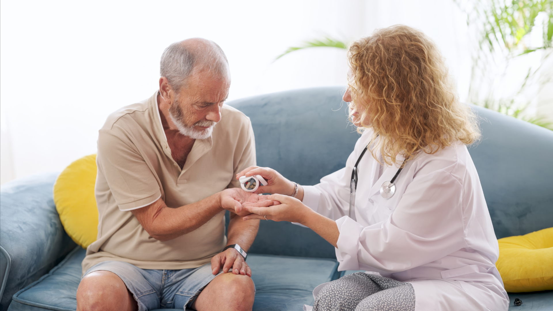 Caregiver checking an older adult's wrist at home on a blue couch