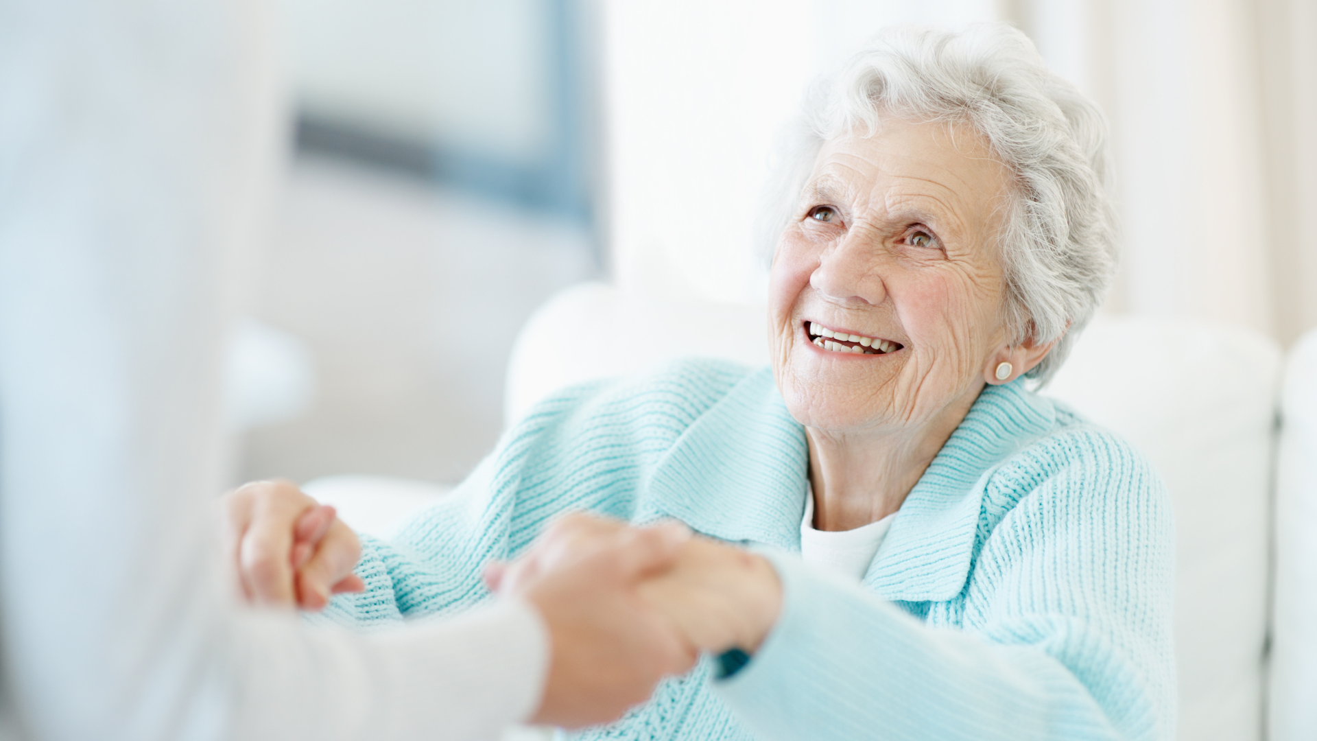 Smiling person in a light blue sweater holding hands with someone in a bright room