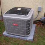 A large air conditioner is sitting on top of a concrete platform in front of a house.