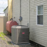 An air conditioner is sitting on the side of a house next to a window.