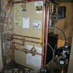 A boiler is sitting in a room next to a wall with copper pipes.