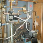 A boiler with a lot of wires coming out of it is in a room.