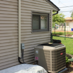 An air conditioner is sitting on the side of a house next to a window.