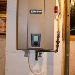 A water heater is hanging on a wall next to a pipe.