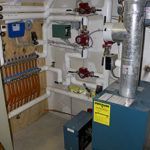 A blue boiler is sitting in a room next to a wall.