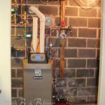 A boiler is sitting in a room next to a brick wall.