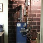 A blue water heater is sitting in a room next to a brick wall.