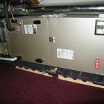 A large air conditioner is sitting on top of a carpeted floor in a room.