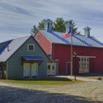 A red barn and a blue barn are sitting next to each other on a dirt road.