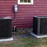 Two air conditioners are sitting in front of a red house.