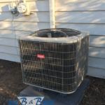 An air conditioner is sitting on top of a concrete block in front of a house.